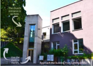 A Picture of the event location.  Text says "The Church Entrance is up here, use the stairs or lift, approach the building from Loretto Straße".  The image shows a door and a lift to the left of the building.